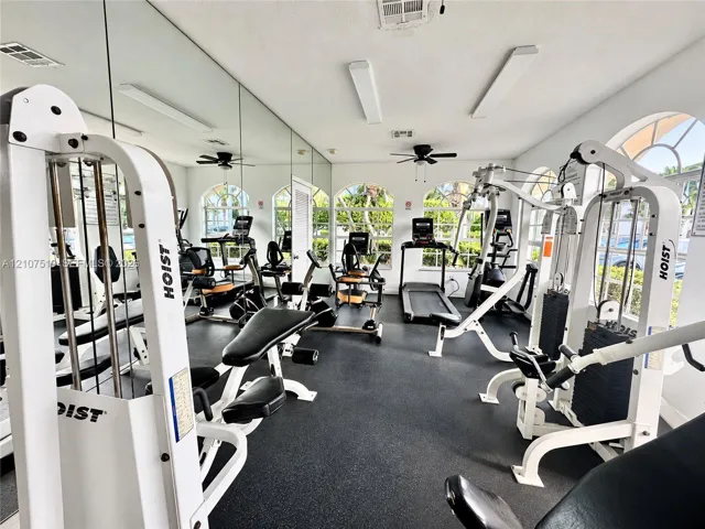 Fitness facility featuring rubberized flooring, floor-to-ceiling wall mirrors, arched windows, and integrated ceiling fans