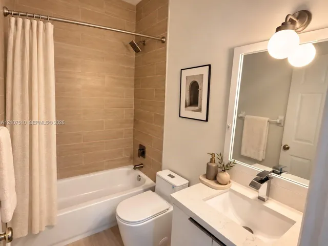 Bathroom featuring a tub-shower combination with horizontal tile surround, a white vanity with a composite countertop, an integrated rectangular sink, a dual-globe wall-mounted light fixture, and metallic hardware