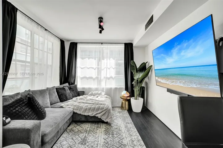 Living space featuring wood-finish flooring, multiple windows with white sheer panels, and track lighting