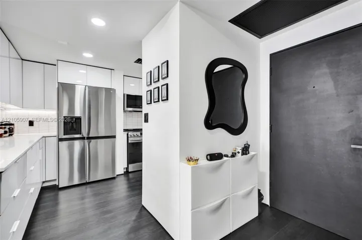 Contemporary kitchen featuring high-gloss white cabinetry, stainless steel appliances, integrated microwave, and dark-toned flooring
