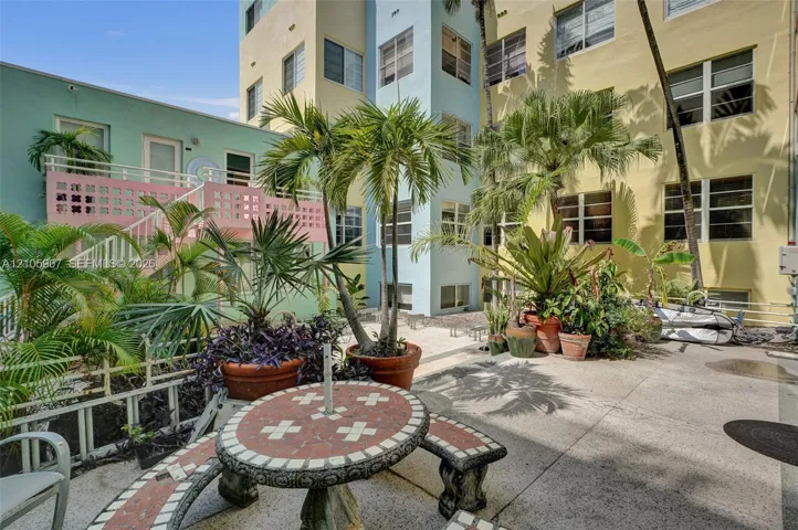 Exterior courtyard featuring a concrete patio, pastel-toned building facade, integrated staircase with decorative breeze block railing, and mature palm trees