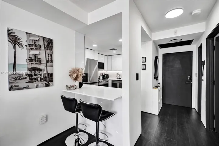 Interior entry featuring dark wood-finish flooring, a built-in white peninsula counter, flat-panel white cabinetry, and stainless steel appliances