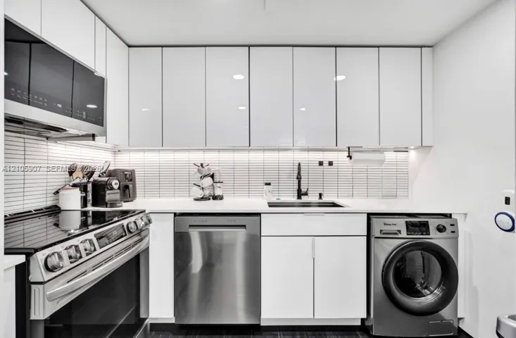 Sleek kitchen featuring high-gloss white cabinetry, linear tiled backsplash, integrated stainless steel appliances, solid surface countertops, and under-cabinet lighting