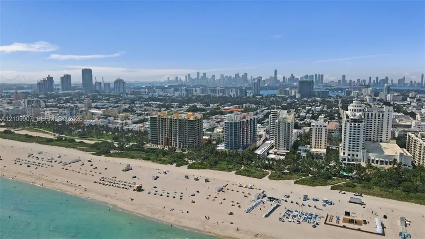 Aerial perspective featuring direct oceanfront access, pristine sandy shoreline, and a panoramic skyline backdrop