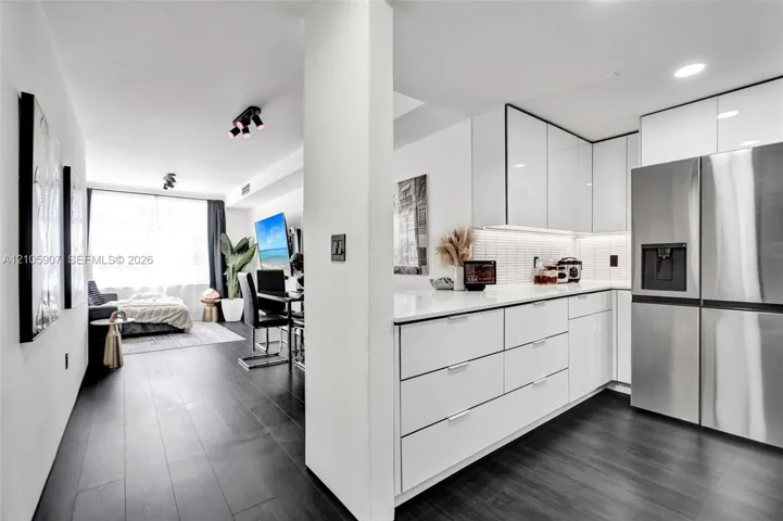 Kitchen featuring high-gloss white cabinetry, white stone countertops, a tiled backsplash, and stainless-steel refrigerator
