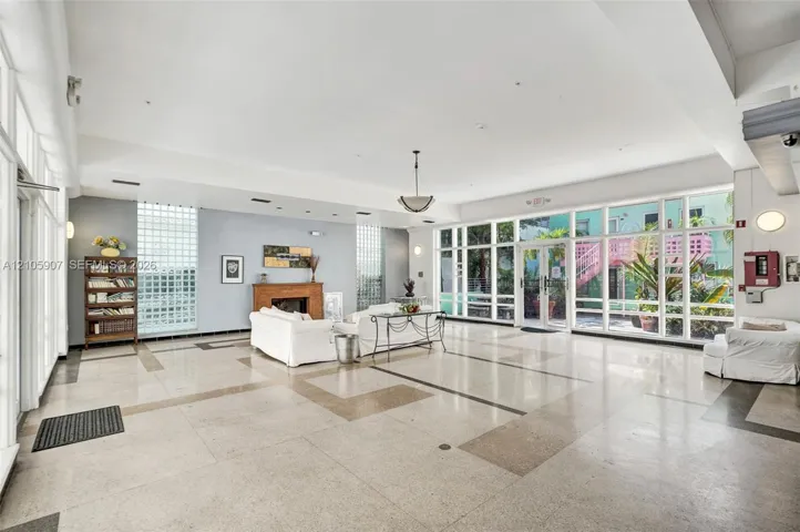 Expansive open-concept room featuring high ceilings, polished stone flooring with geometric inlay, floor-to-ceiling glass panel walls, dual glass block windows, and a built-in wood-finished fireplace