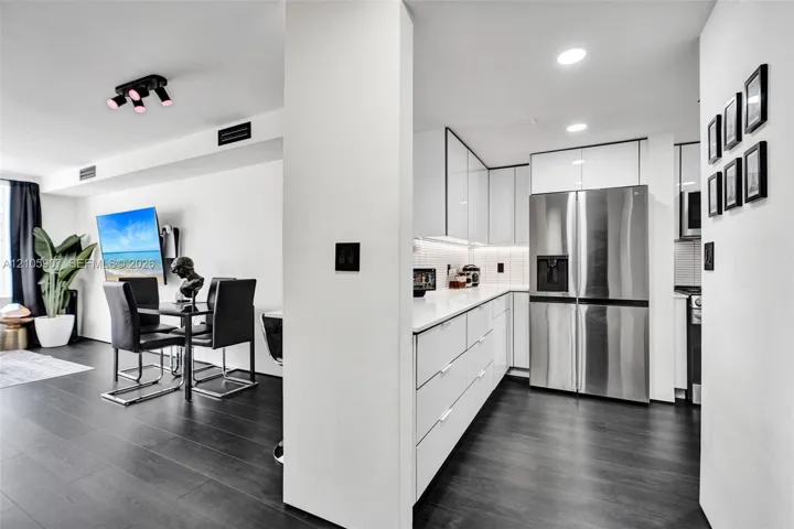 Contemporary kitchen featuring flat-panel white cabinetry, solid-surface countertops, recessed ceiling lighting, and stainless steel French-door refrigerator, finished with dark wood-finish flooring