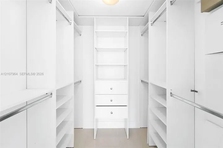 Custom walk-in closet featuring white built-in shelving, triple stacked drawers with hardware, multiple hanging rods, and wood-finish flooring