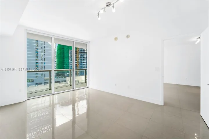 Large-format tile flooring, floor-to-ceiling glass sliding doors, covered balcony with metal railing, and multi-directional track lighting