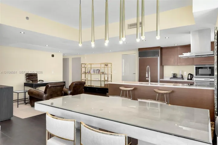 Open concept kitchen featuring dark wood-finish cabinetry, built-in stainless steel appliances, a center island with a stone countertop, and custom multi-pendant lighting