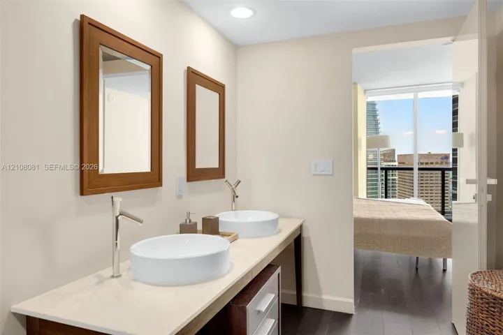 Dual-basin vanity featuring white vessel sinks, quartz countertops, chrome high-arc faucets, and wood-framed mirrors