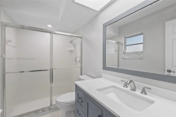 Bathroom featuring a gray vanity with a stone countertop, an integrated undermount sink, a framed mirror, and a walk-in shower with a sliding glass enclosure