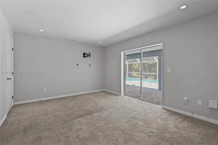 Neutral wall finishes, recessed lighting, wall-to-wall carpeting, and sliding glass doors opening to a screened-in lanai with a pool