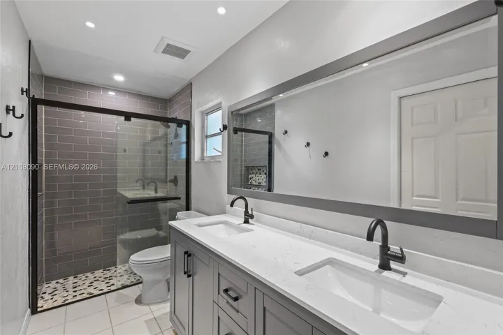 Double vanity with quartz countertop, undermount sinks, matte black faucets, and a framed mirror, complemented by a walk-in shower with gray subway tile walls and a pebble-stone floor