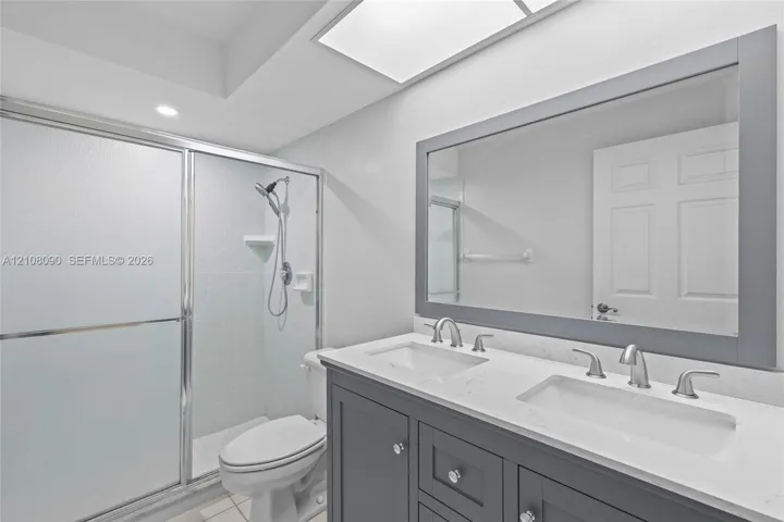 Dual-sink vanity with a solid-surface countertop and shaker-style cabinetry, framed wall mirror, and walk-in shower with a sliding glass door and handheld shower fixture