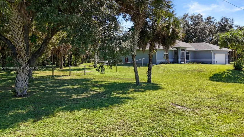 Expansive yard featuring mature palm and shade trees, a fenced perimeter, and a detached residence with a multi-car garage