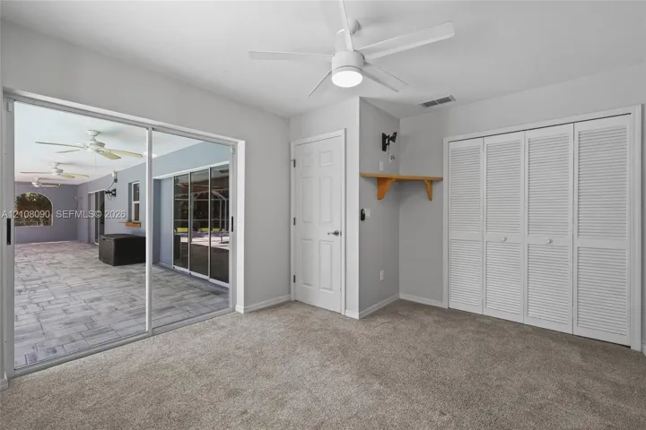 Room featuring neutral carpeting, sliding glass doors, white louvered-style closet doors, and a ceiling fan with integrated lighting