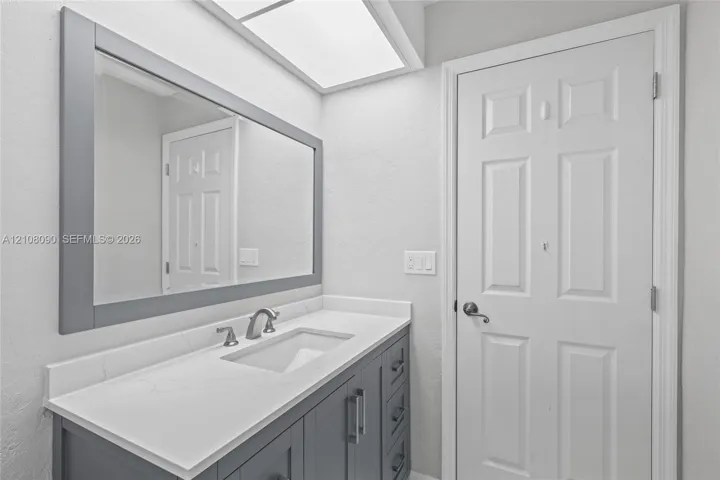 Vanity featuring a dark gray cabinet, white countertop with an integrated rectangular sink, wall-mounted mirror with a dark gray frame, brushed nickel faucet, and recessed ceiling lighting