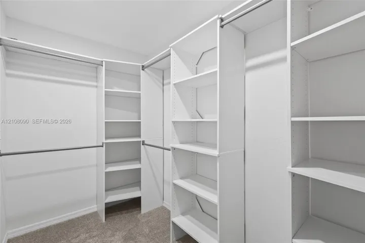 Walk-in closet featuring white built-in shelving towers, multiple horizontal hanging rods, and neutral carpeting