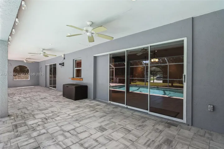 Covered outdoor patio featuring paver flooring, multiple ceiling fans, recessed lighting, and large sliding glass doors providing visibility of the enclosed pool area