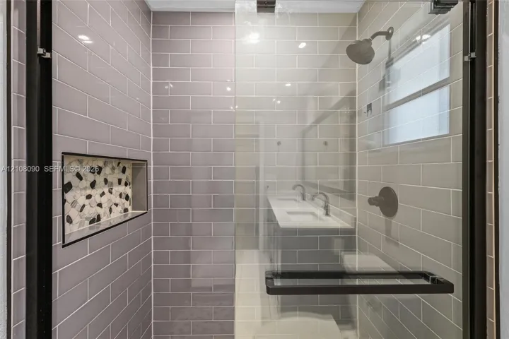 Walk-in shower featuring grey subway tile, a decorative stone-mosaic inlay niche, frameless glass enclosure, and matte black fixtures
