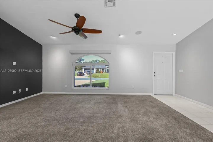 Interior space featuring wall-to-wall carpeting, recessed ceiling lighting, a ceiling fan, an arched window, and a contrasting accent wall