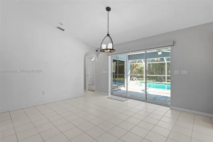 Living area featuring ceramic tile flooring, vaulted ceilings, an arched entryway, decorative pendant lighting, and sliding glass doors providing outdoor access
