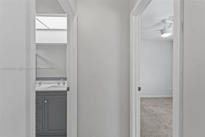 Bathroom featuring a gray vanity with a dual-basin countertop, integrated skylight, and bedroom with a ceiling-mounted light fixture