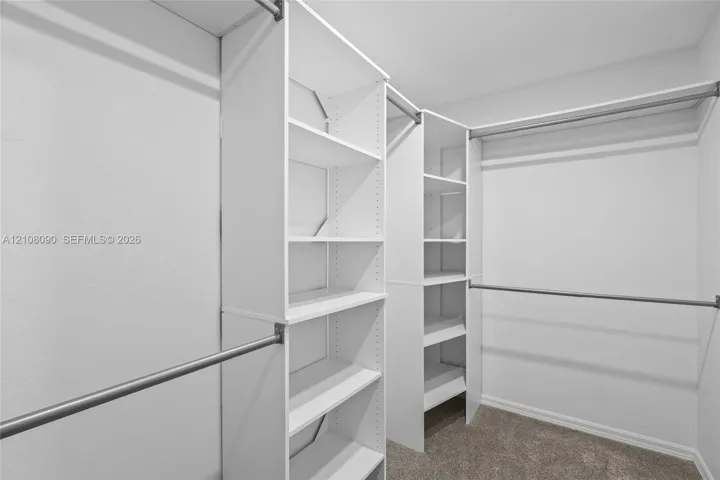 Walk-in closet featuring white built-in shelving towers, adjustable open-tier storage, and multiple metal hanging rods
