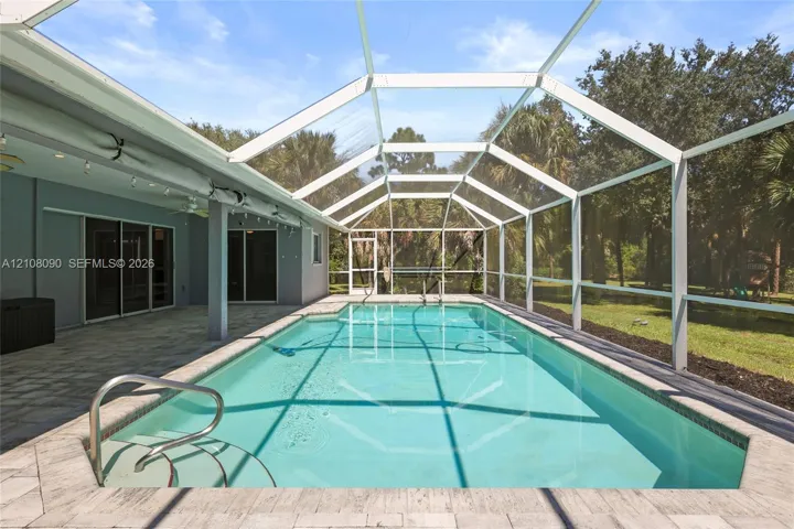 Screened-in patio featuring a rectangular swimming pool, integrated entry steps, paver decking, and metal pool handrails