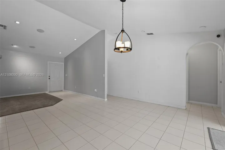 Vaulted ceilings with recessed lighting, neutral ceramic tile flooring, architectural arched entryway, and a tiered metal and wood-finish pendant light fixture