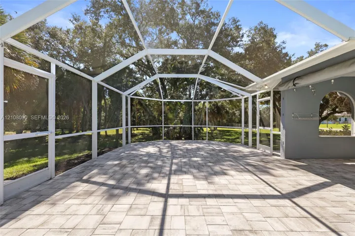 Screened-in patio featuring brick-style paver flooring, white structural framing, and an arched wall opening