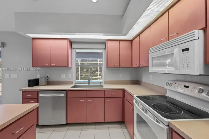 Kitchen featuring wood cabinetry, solid surface countertops, stainless steel dishwasher, integrated electric range with overhead microwave, and ceramic tile flooring