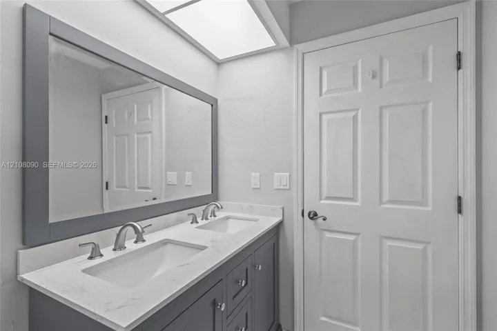 Double vanity featuring a light-toned countertop, dual rectangular undermount sinks, polished metal widespread faucets, and a framed mirror