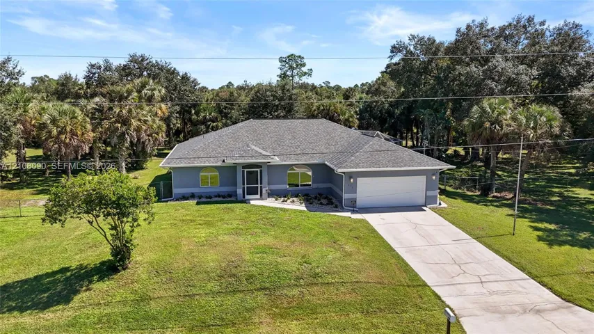 Single-story residence featuring a shingle roof, arched window detailing, two-car garage, and concrete driveway, situated on a sprawling lot with mature trees