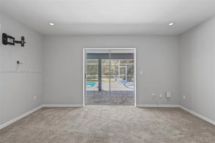 Neutral wall color, wall-to-wall carpeting, recessed ceiling lighting, and sliding glass doors with exterior screen enclosure access