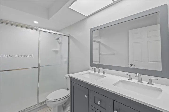 Dual-sink vanity with a light-toned countertop, framed wall mirror, and walk-in shower featuring a sliding glass enclosure