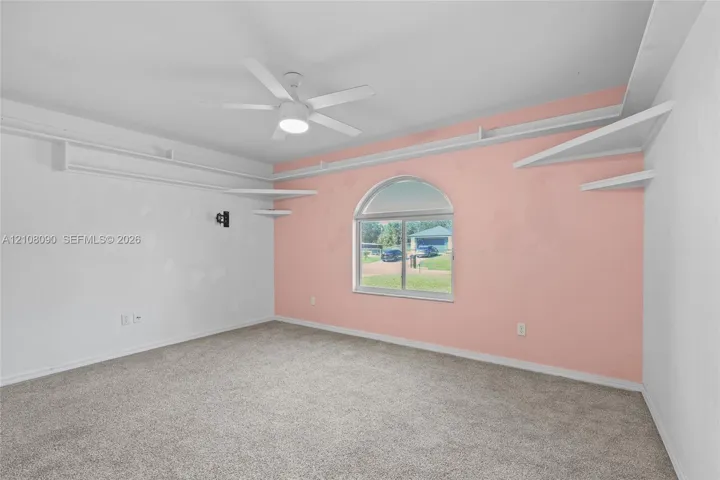 Room featuring carpeting, a ceiling fan with integrated lighting, multiple wall-mounted tiered shelves, and an arched window
