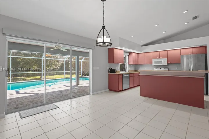 Kitchen featuring cabinetry, a breakfast bar, and stainless steel appliances, paired with tiled flooring and sliding glass doors revealing a screened-in pool and patio