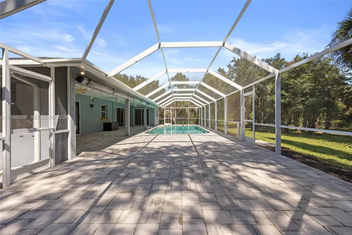 Enclosed pool area featuring a paved deck, screened-in structure, and exterior access points