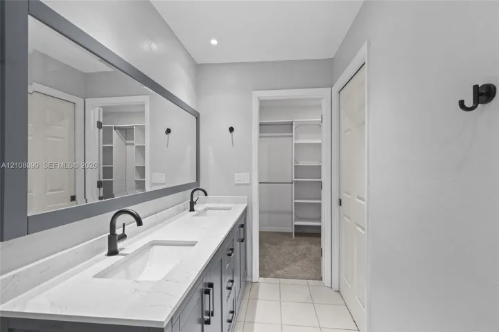 Dual-sink vanity with white stone-finish countertop, matte black fixtures, full-width framed mirror, and built-in closet shelving