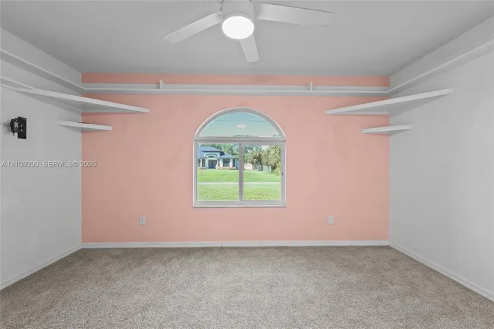Room featuring wall-to-wall carpeting, a center ceiling fan with integrated lighting, and multiple tiers of built-in shelving flanking an arched window