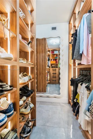 Walk-in closet featuring custom wood-finish shelving with integrated vertical lighting, polished tile flooring, and a full-length mirror with a decorative wave-edge frame