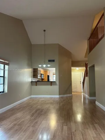 Vaulted ceilings, wood-finish flooring, three-light chandelier, pass-through kitchen opening, and wooden stair railing