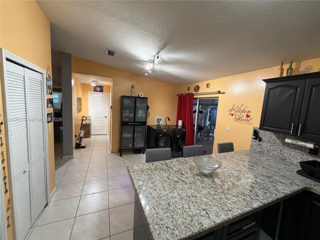 Kitchen featuring stone-finish countertops, dark cabinetry, ceramic tile flooring, and integrated laundry area with dual folding doors