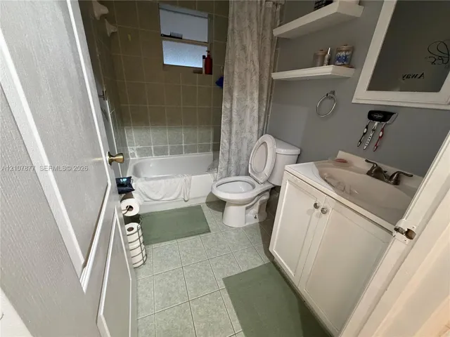 Bathroom featuring a white vanity cabinet with an integrated sink, porcelain tile flooring, a tub-and-shower combination with tile surround, and two built-in wall shelves