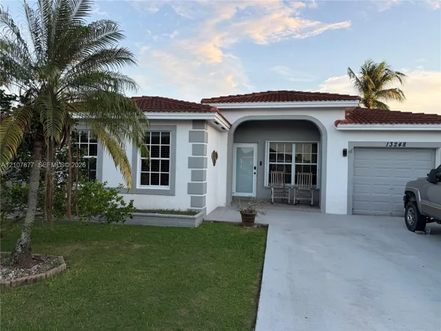 Single-story exterior featuring a red tile roof, arched entryway, quoined corner detailing, and a concrete driveway