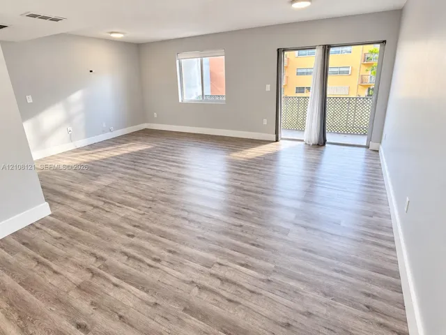 Open interior space featuring wood-finish flooring, sliding glass doors, a lattice-enclosed balcony, and neutral wall tones
