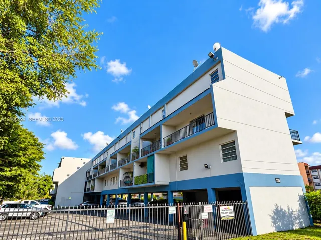 Multi-story structure featuring a stucco exterior with tiered balconies, metal railings, louvered windows, and covered ground-level parking
