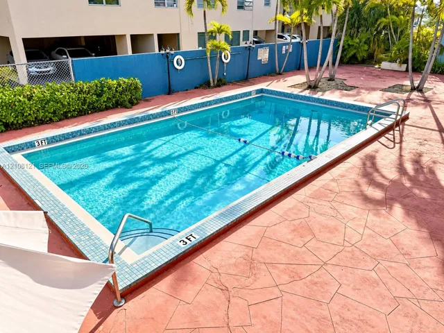 Rectangular in-ground swimming pool featuring a tiled waterline, metal handrails, and a stamped concrete deck